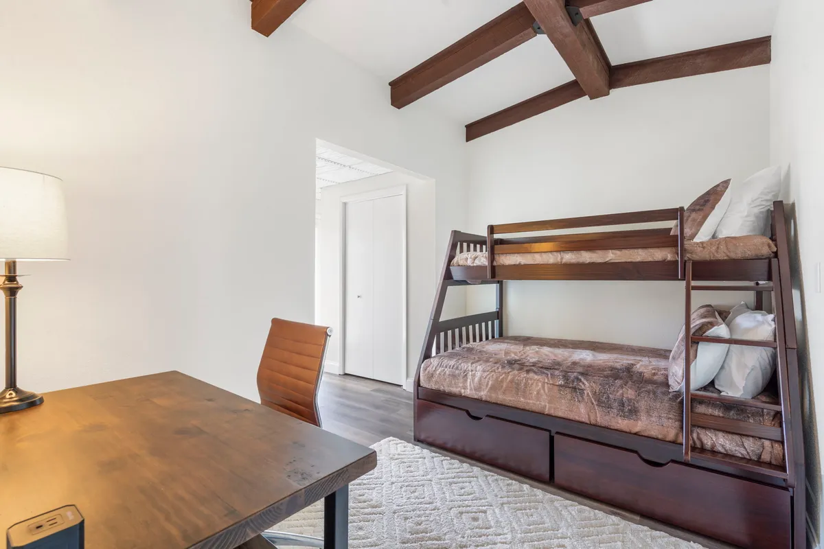 A cozy second bedroom with a twin-over-full bunk bed, a simple desk for reading or studying, and a lamp that creates a warm, inviting glow. The space is tailored for both relaxation and functional use, making it ideal for kids or guests.