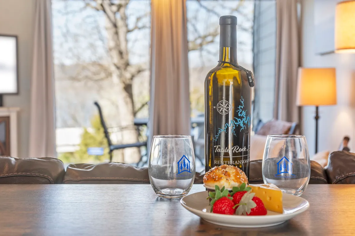 A cozy interior setting featuring a wine bottle, cheese plate, strawberries, and glasses arranged for two on a small table. The warm lighting and relaxed mood evoke intimacy and the enjoyment of local flavors together.