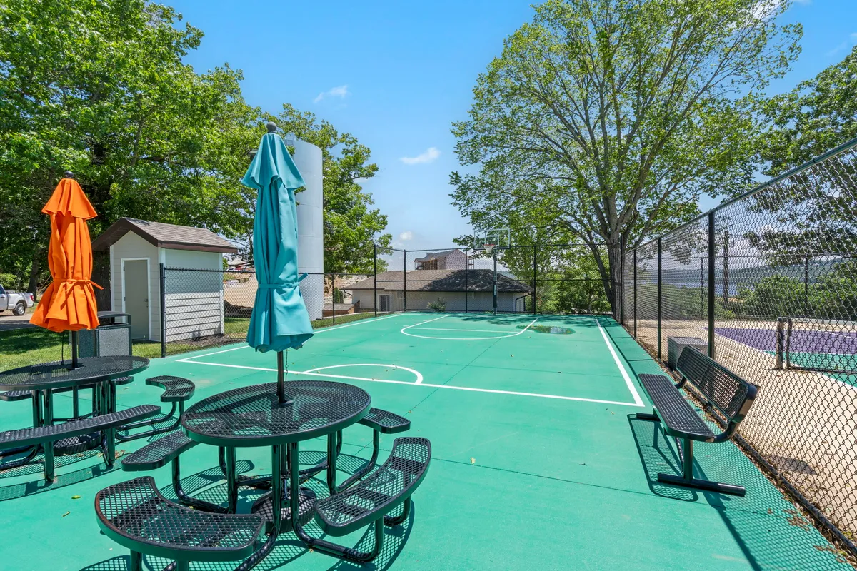A basketball court bustling with activity, surrounded by colorful umbrellas and benches, where residents are playing basketball, socializing, and enjoying picnics under a cheerful, sunny sky.