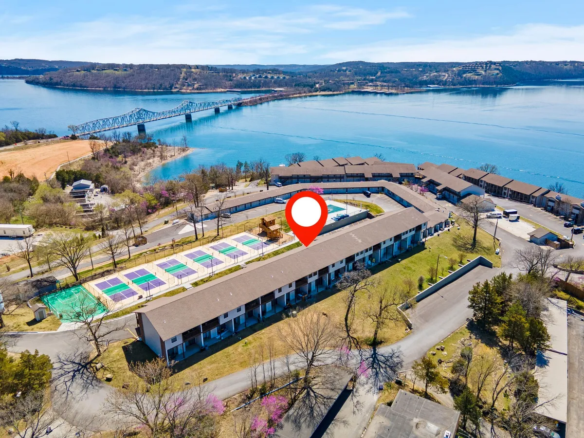 An inviting exterior scene featuring a sparkling swimming pool, well-maintained tennis courts, and a serene lake framed by lush greenery. The image captures the vibrant community spaces and natural beauty that surround the condo, with areas for swimming, tennis, and relaxing by the water all visible in one shot.