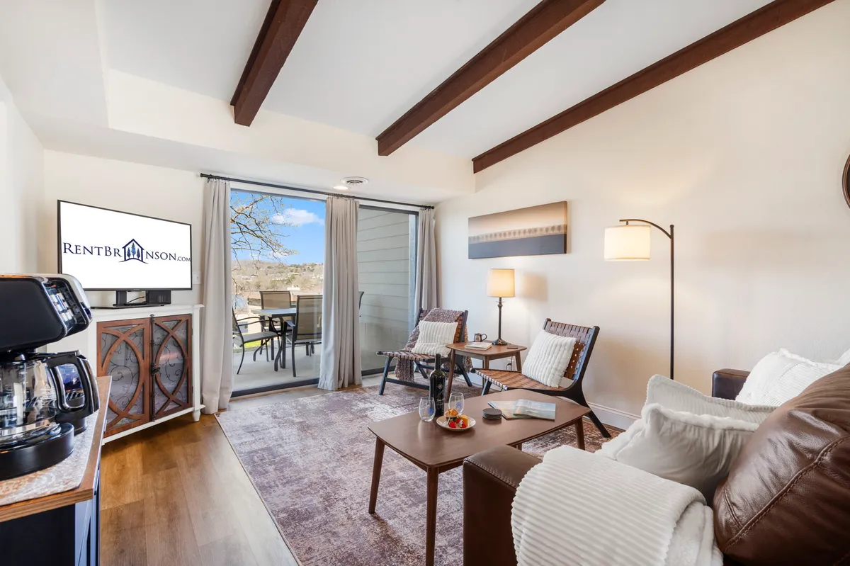 A comfortable seating area with a TV, coffee maker, and balcony access. The arrangement is inviting for lounging, watching TV, or sharing a coffee, with natural light enhancing the cozy, welcoming mood.