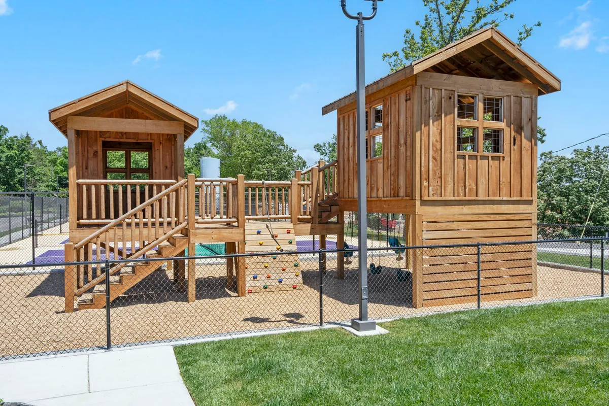 This exterior image features a joyful playground area with imaginative treehouse structures, a colorful climbing wall, and children actively playing. The vibrant equipment and group activity highlight spaces designed for children and social gatherings.