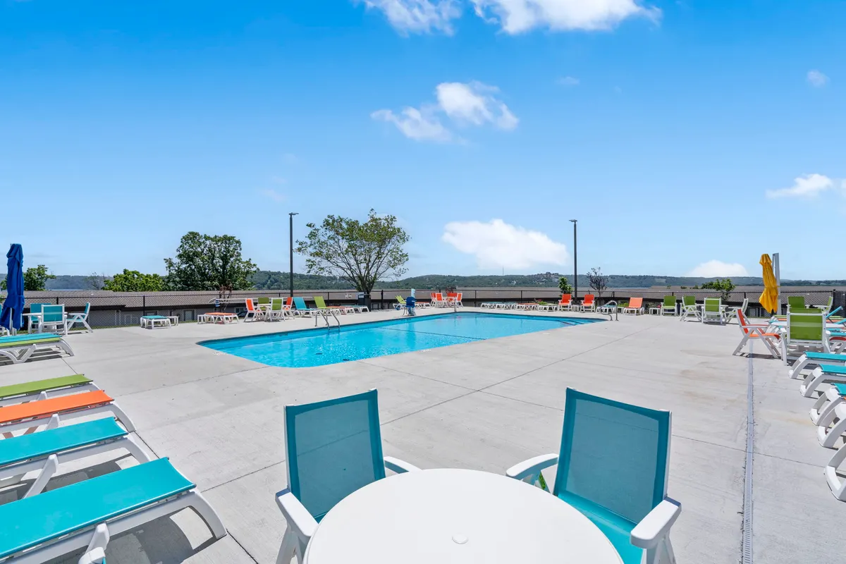 An inviting outdoor swimming pool surrounded by colorful lounge chairs, with a bright blue sky overhead. The lively atmosphere suggests opportunities for sunbathing, swimming, and socializing in warm weather.