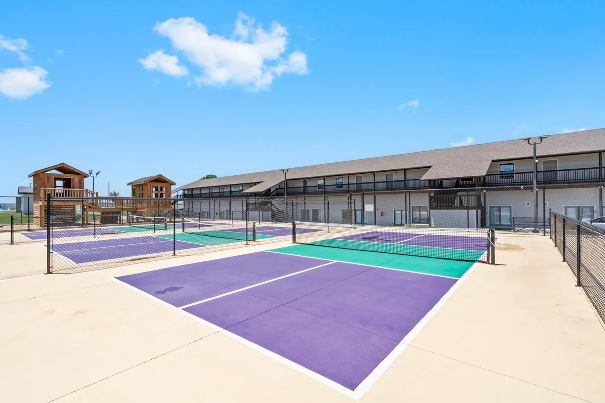 An energetic exterior view of tennis courts with colorful surfaces, surrounded by residential buildings. The scene suggests active recreation, social play, and family-friendly fun onsite.