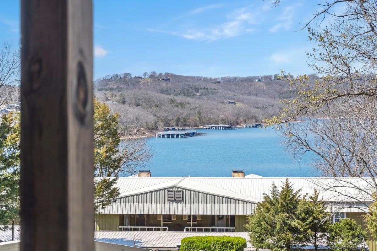A peaceful lake view framed by distant hills and a boathouse, with a tree-lined shore extending into the distance. The water glistens under soft natural light, evoking a tranquil, romantic atmosphere perfect for morning strolls or quiet reflection.