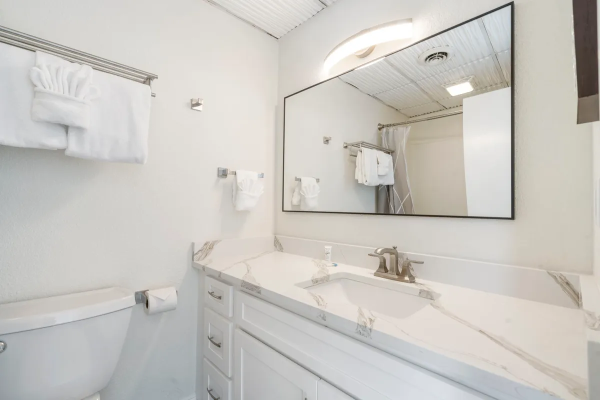 A bright, spa-like bathroom featuring a marble countertop, an expansive mirror, and neatly arranged plush towels. The ambiance is clean and inviting, perfect for unwinding.