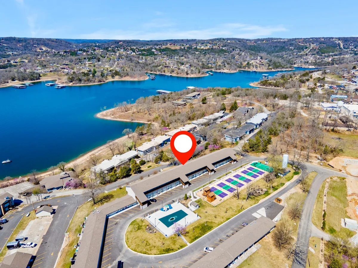 This exterior image shows a vibrant lakeside scene with Table Rock Lake, adjacent residential buildings, a swimming pool, and a colorful area that hints at active outdoor spaces. The setting includes people enjoying swimming, boating, picnicking, and gathering outdoors.