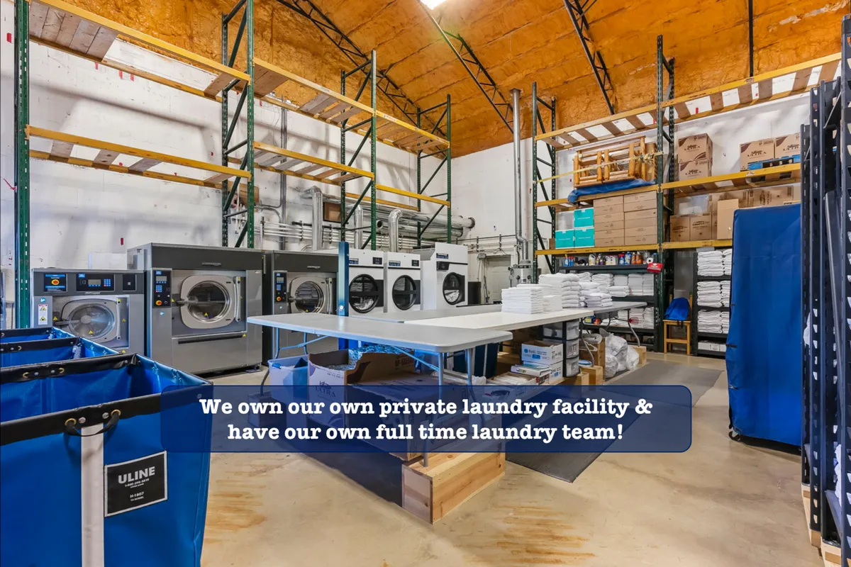 An efficient laundry area with industrial washing machines, folding tables, and organized storage shelves. The scene conveys cleanliness and the professionalism with which linens are handled.