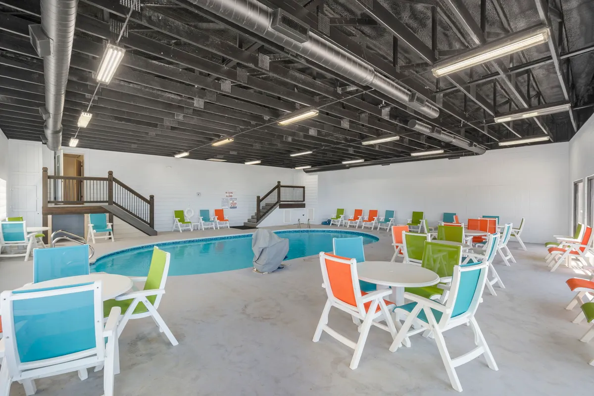 A vibrant indoor pool area featuring colorful lounge chairs and tables. The space is well-lit and designed for swimming, social gatherings, and relaxing, no matter the season.